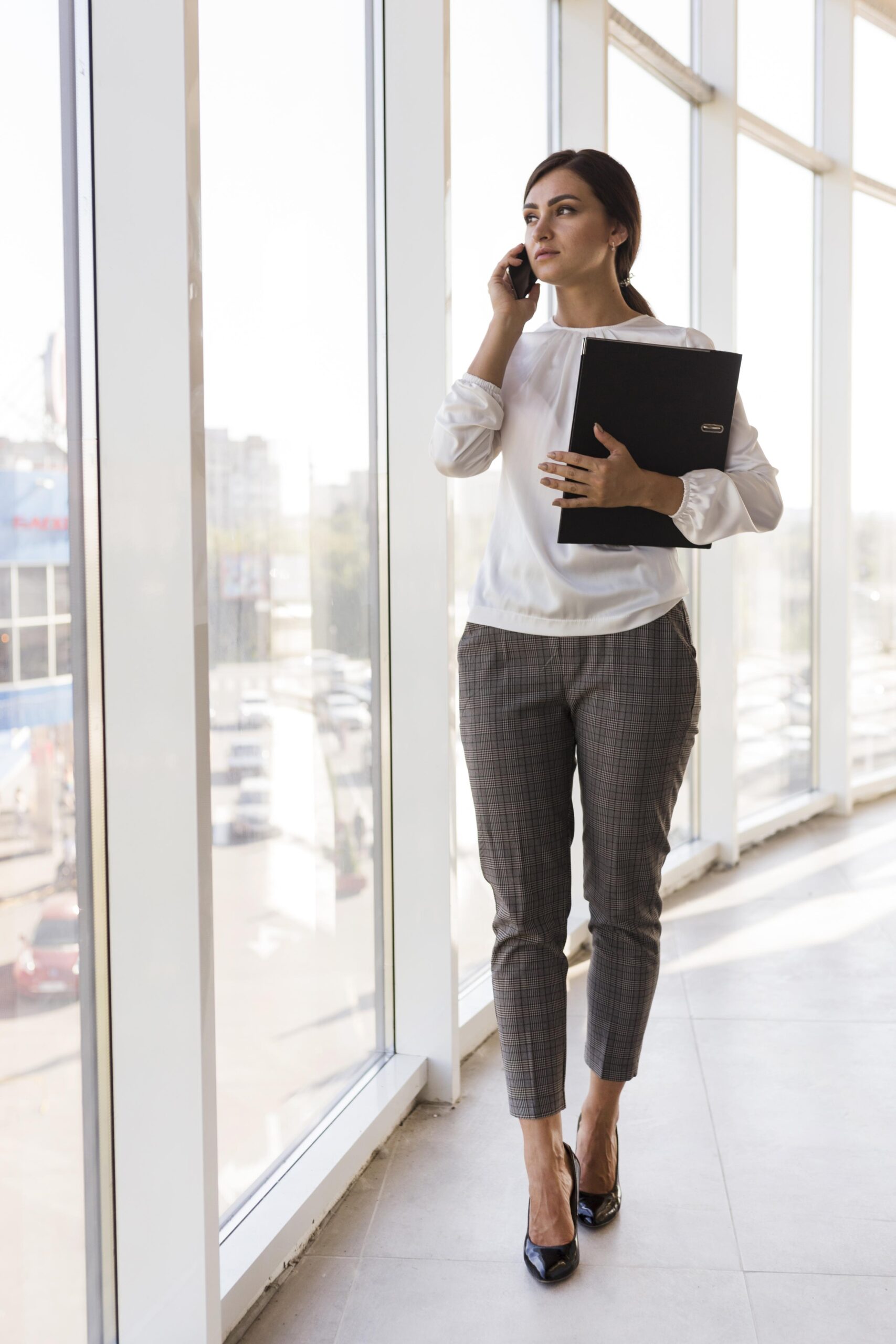front view businesswoman holding binder talking phone